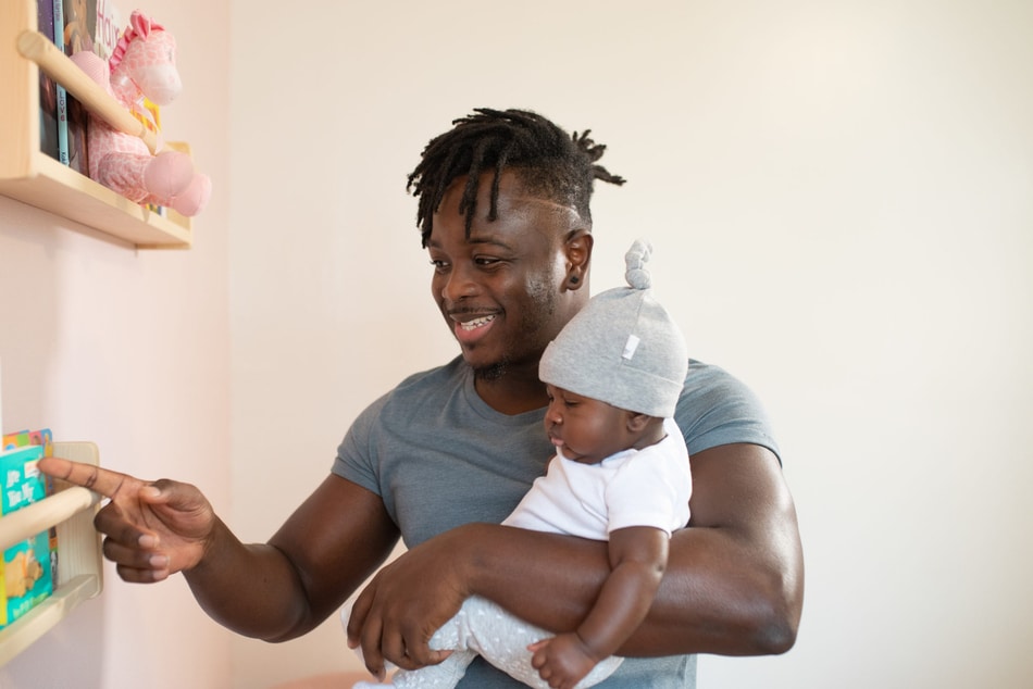 Man pointing to a children's book while carrying his baby