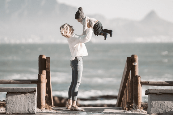 Mother holding a child in the air in front of a body of water