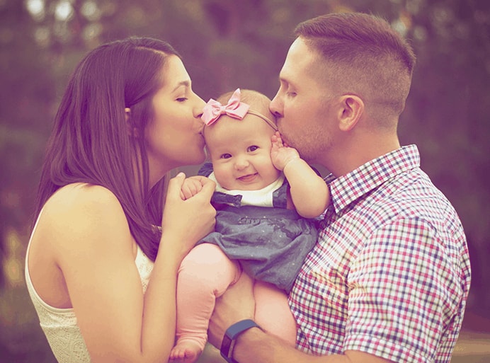 Mother and father holding a baby between them and kissing its head