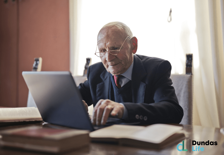 Serious senior man using laptop while sitting at table with books