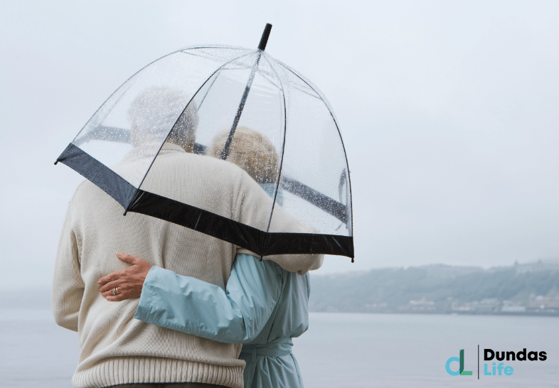 Older couple standing in rain with umbrellas