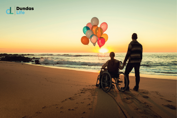 A person in a wheelchair holding balloons on a beach happy about disability insurance.